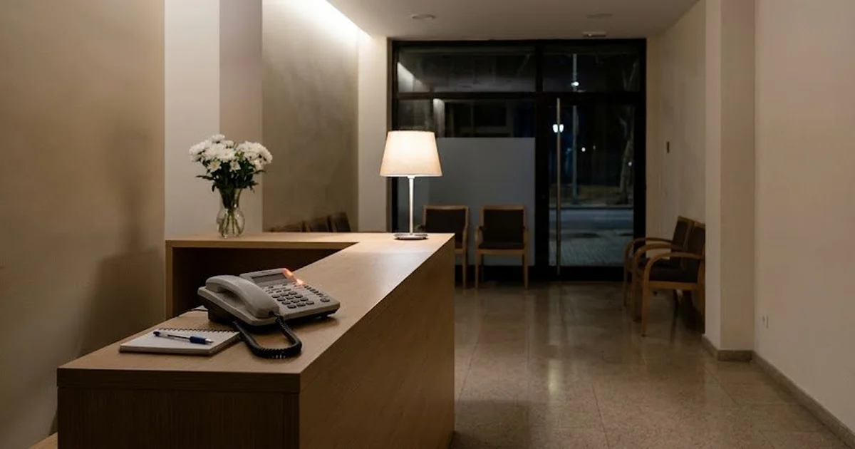 Recepción de un tanatorio de noche, vacía y en silencio, con un teléfono iluminado sobre el mostrador
